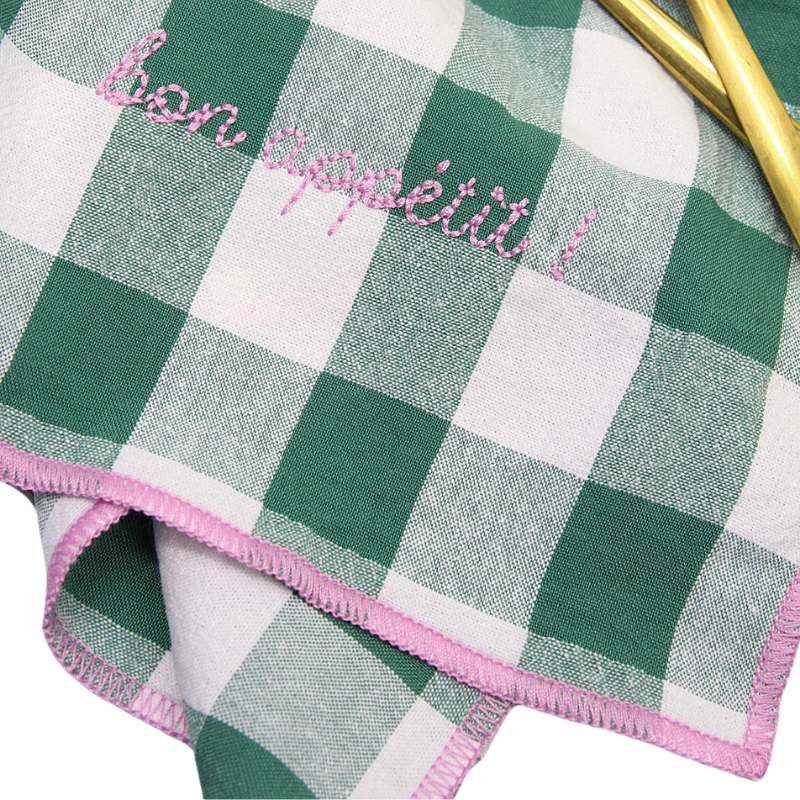 Green and white checkered napkin with pink trim and 'bon appetit' embroidery.
